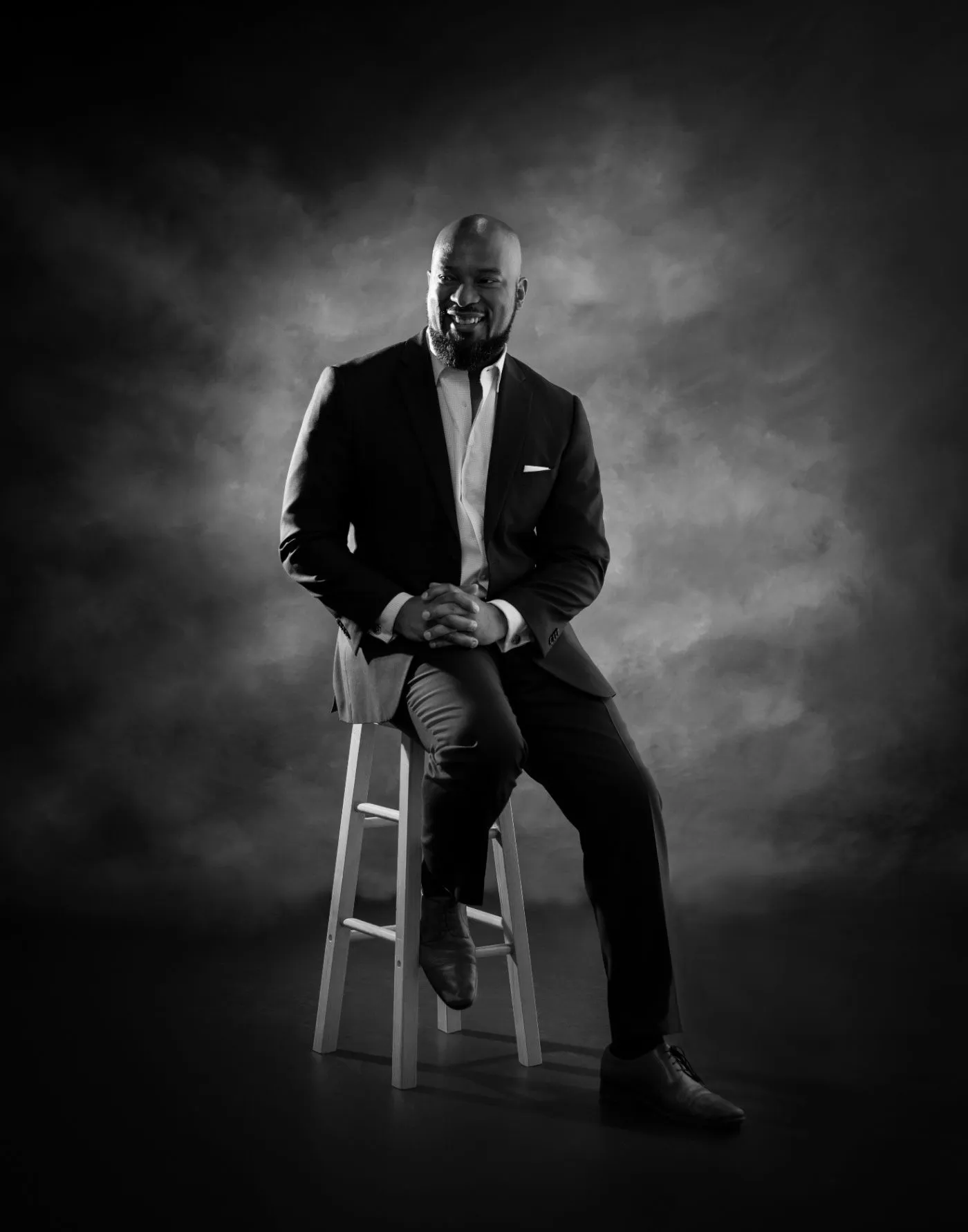 John Miller seated in a suit, smiling in a studio portrait